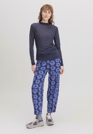 Donkerblauwe top met lange mouwen en een fitted ontwerp, gecombineerd met losse, bloemenpatroon blauwe broek. Grijze sneakers met roze accenten maken de outfit compleet.
