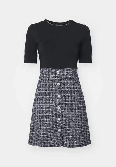 Haut noir à manches courtes avec un corsage ajusté, associé à une jupe texturée bleu marine avec un devant boutonné. Le tissu présente un motif tissé.