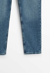Jambes de jeans en denim bleu avec coupe droite et coutures visibles sur fond blanc.