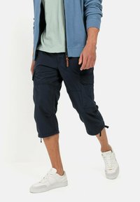 Marine cargoshorts met zijzakken en verstelbare zoom, gemaakt van lichtgewicht stof. Gecombineerd met een lichtblauw top en witte sneakers.