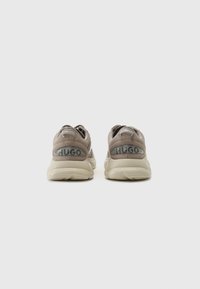 Beige athletic shoes featuring a suede and mesh upper, round toe, prominent heel cushioning, and a logo detail at the back.