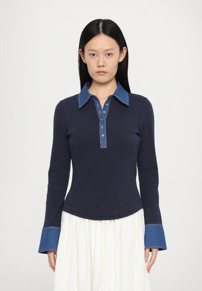 Tricou polo cu manșon lung de culoare bleumarin, cu guler și manșete din denim, având un închidere cu butoane și o tivă curbată. Material moale, texturat.