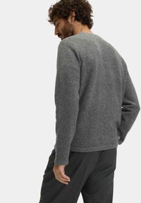 Grauer Wollpullover mit rundem Halsausschnitt und langen Ärmeln, der eine weiche Textur und eine lockere Passform aufweist. Kombiniert mit dunkelgrauen Hosen.