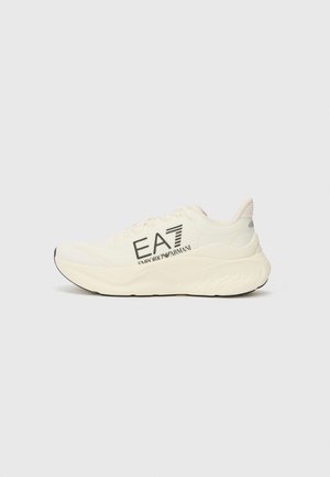 Light cream athletic shoe with textured upper, black outsole, and prominent EA7 branding in dark lettering on the side.