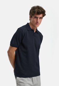 Mørkeblå kortermet polo-skjorte med strukturert stoff, standard krage, ribbede mansjetter og kant. Enkel design uten mønstre eller logoer.