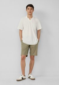 Witte gestructureerde korte mouw polo, lichtgroene shorts, staand op een witte achtergrond, gecombineerd met witte sneakers met bruine accentueringen.