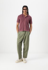 Korte mouwen kastanjekleurige gebreide shirt met een kraag, houten knopen, gecombineerd met losse olijfgroene broeken en crèmekleurige sneakers.