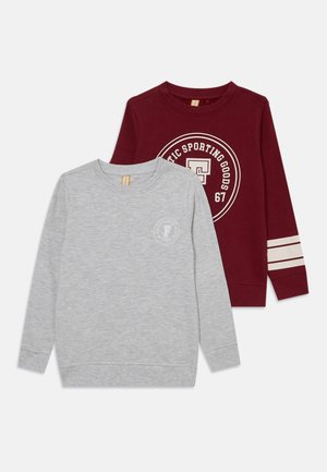 Zwei Sweatshirts mit langen Ärmeln: eines in Grau mit einem runden Logo und eines in Kastanienrot mit cremefarbenen Streifen und einem runden Logo. Beide bestehen aus weichem Stoff.