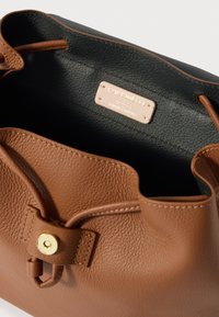 Καφέ δερμάτινη τσάντα τύπου κουβά με υφή, διαθέτει κλείσιμο με χρυσό κουμπί και μαύρη εσωτερική ετικέτα που υποδηλώνει ιταλικό δέρμα.