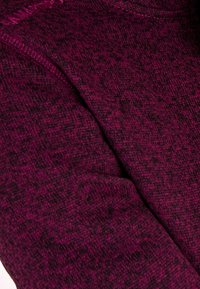 Acercamiento de una tela de punto texturizada en magenta oscuro con sutiles patrones negros y costura visible a lo largo de la costura.