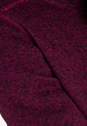 Acercamiento de una tela de punto texturizada en magenta oscuro con sutiles patrones negros y costura visible a lo largo de la costura.