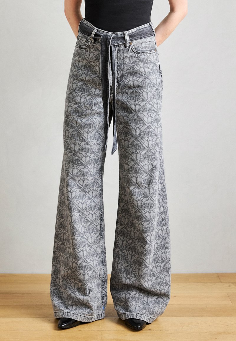 Wide-leg denim trousers in gray, featuring a geometric pattern, high waist, loose fit, and a tie at the waist. Smooth texture and denim weave.