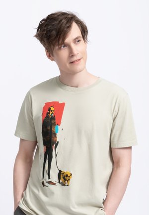 T-shirt in cotone verde chiaro con una stampa artistica di una persona con un cane, su uno sfondo rosso, con accenti neri e gialli.