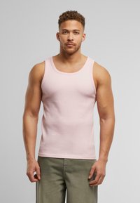 Lys pink ribbet tanktop med rund halsudskæring, tætsiddende pasform og blød tekstur, parret med olivengrønne bukser.