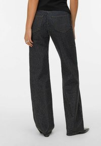 Crne trapezice s točkicama, izrađene od teksturiranog materijala i s pet džepova. Vidljivi šavovi i blagi sjajni naglasci.