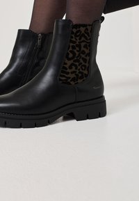 Černé kožené kotníkové boty se zvířecím potiskem na textilní boční části, s robustní podrážkou a zipovým uzávěrem pro snadné obouvání.