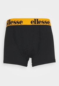 Svarta boxer shorts med ett tjockt gult elastiskt midjeband som har texten "ellesse" i svart. Slät textur, åtsittande design.