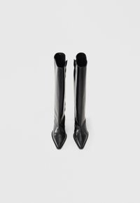 Bottes montantes jusqu'aux genoux en cuir noir avec une pointe effilée et une silhouette fine. Elles présentent une texture lisse, un design structuré et une fermeture zippée.