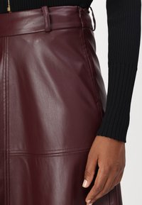 Jupe en cuir bordeaux à taille haute, texture lisse et panneaux cousus. Accompagnée d'un haut noir à manches longues côtelées.