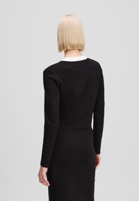 Black, fitted long-sleeve top with a white collar. Smooth texture, cropped design, plain fabric without patterns, back view.
