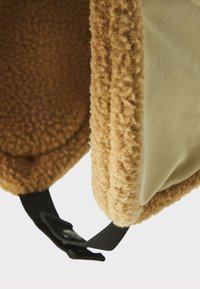 Close-up of beige fleece fabric with soft texture and black strap with buckle detail on light background.