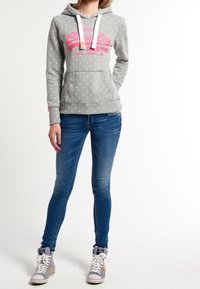 Felpa grigia con pois e logo rosa, con cordini bianchi, tasca frontale, abbinata a jeans blu e sneaker alte grigie.