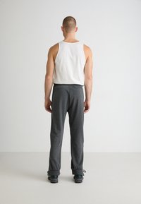 Graue Sporthose mit seitlichen Taschen, elastischem Bund und Kordelzug; kombiniert mit einem schlichten weißen Tanktop.