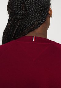 Bordeauxrode trui met een ronde hals, gestructureerde brei en een subtiel accent aan de kraag met rode, witte en zwarte strepen.