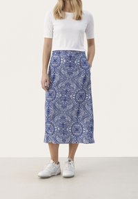 Maxi-Rock mit blauem Muster und komplexen Designs, aus Stoff gefertigt, kombiniert mit einem weißen enganliegenden Oberteil und weißen Sneakers.
