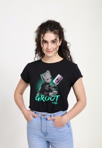 Černé tričko s krátkým rukávem, které má na sobě grafiku Groota držícího kazetu, doplněnou tyrkysovými akcenty a s nápisem "GROOT" vytištěným pod obrázkem.