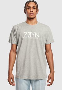 Pilkas medvilninis marškinėlis su baltu tekstu, kuris sako "ZAYN ROOM UNDER THE STAIRS." Klasikinis apvalus kaklas ir trumpomis rankovėmis.