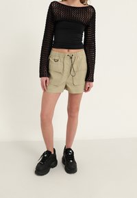 Top negro de punto de manga larga con un escote amplio, combinado con pantalones cortos cargo color caqui con cintura ajustable y múltiples bolsillos. Zapatillas negras.