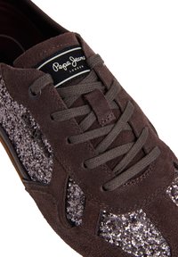 Baskets en daim marron avec des lacets marron foncé, des panneaux latéraux pailletés et une étiquette noire indiquant Pepe Jeans London sur la languette.