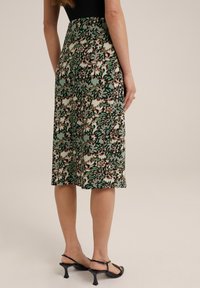 Sukně ke kolenům s zeleným květinovým vzorem na strukturované tkanině, s přiléhavým pasem a bočními rozparky. Kombinováno s černými sandály.