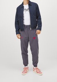 Jeansjacka, vit t-shirt med grafisk design, grå joggerbyxor med röd logotyp och rosa sneakers. Slim fit med elastiska ärmslut på byxorna.