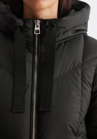 Giacca a vento nera con cappuccio, caratterizzata da una zip argentata, accenti del colletto con marchio e texture trapuntata con cuciture tono su tono.