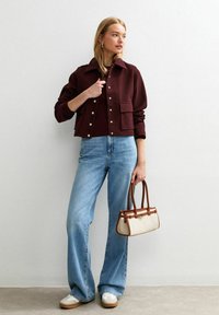 Burgunderfarbener Cropped-Blazer mit goldenen Knöpfen, hellblaue Schlagjeans und eine beige Handtasche mit braunen Griffen. Bequeme Schuhe runden den Look ab.