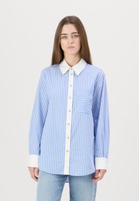 Camicia a righe blu e bianche con colletto bianco, chiusura a bottoni sul davanti e taschino sul petto. Maniche lunghe con polsini bianchi.