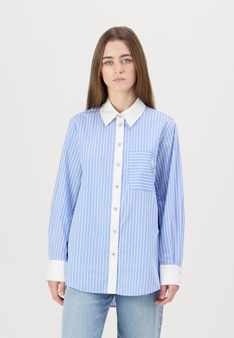 Camicia a righe blu e bianche con colletto bianco, chiusura a bottoni sul davanti e taschino sul petto. Maniche lunghe con polsini bianchi.