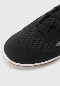 Black athletic shoe with a textured mesh upper, perforated detailing, and a smooth rubber toe cap. Features black laces and white midsole.