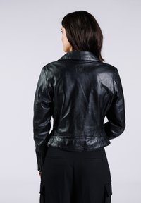 Chaqueta de motociclista de cuero negro con un diseño ajustado, textura elegante y un sutil logotipo en la parte posterior. Presenta mangas con cremalleras.