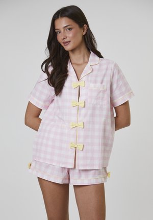 Rosa-weiß kariertes Pyjama-Set mit kurzen Ärmeln, gelber Paspelierung und Schleifenakzenten an den Knöpfen und Seiten der Shorts.