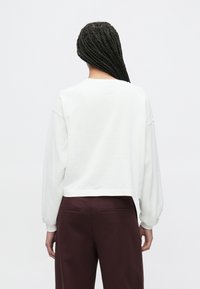 Krótka biała bluza z długimi, obszernymi rękawami, z okrągłym dekoltem. W połączeniu z bordowymi spodniami z wysokim stanem. Prosty design.