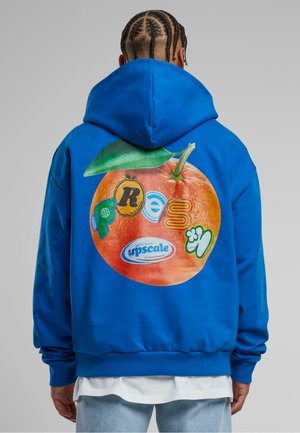 Niebieska bawełniana bluza z kapturem z dużą pomarańczową grafiką na plecach, zawierającą różne kolorowe logo oraz zielony detal liścia. Rękawy i dół wykończone ściągaczem.