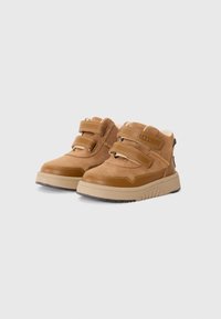 Bottes en suede marron avec deux sangles Velcro, col rembourré et semelle en caoutchouc épaisse. Caractéristiques incluent des surpiqûres contrastées et une pointe renforcée.