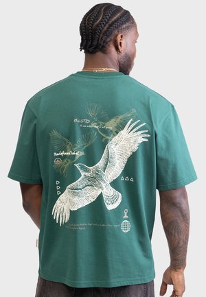 Grünes Baumwoll-T-Shirt mit weißen Vogelgrafiken und Text auf der Rückseite. Kurze Ärmel, Rundhalsausschnitt und lässiger Schnitt mit minimalen Akzenten.