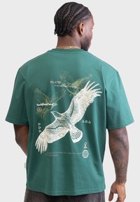T-shirt en coton vert avec un motif artistique d'oiseaux et du texte au dos, à manches courtes et coupe décontractée.