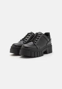 Zwarte platform schoenen van glanzend synthetisch materiaal, met een ronde neus, vetersluiting aan de voorkant en een dikke, geribbelde zool.