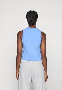 Ljusblå ärmlös topp med rund halsringning, kortad design och mjukt tyg. Kombinerad med ljusgrå, löst sittande byxor.