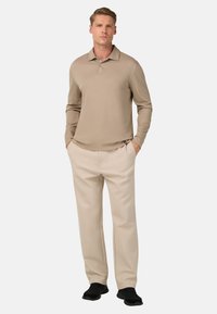 Polo shirt beige a maniche lunghe con colletto piatto, due bottoni, abbinato a pantaloni beige chiaro e sneakers nere. Tessuto liscio, vestibilita' casual.
